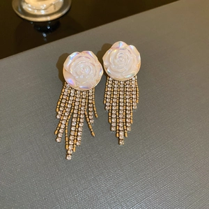 Close-up of white rose petal earrings with sparkling crystal tassels on gold chains