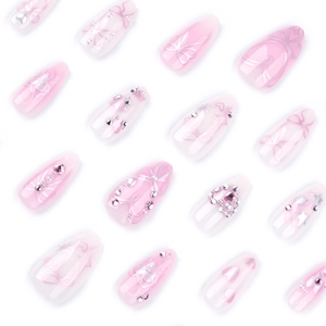 Pink almond press-on nails with silver bows, crystal hearts, and pearl accents on white base