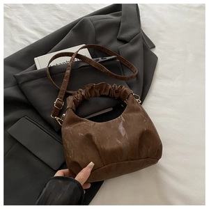 Detailansicht der braunen Crescent-Tasche mit Raffungen auf einem Blazer mit Goldbeschlägen