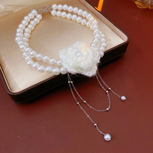Close-up of double-layer pearl necklace with knitted flower and silver tassel in a box