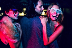 Three people wearing LED star and shutter glasses in a vibrant neon party atmosphere