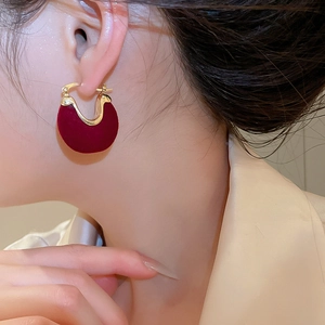 Close-up of elegant burgundy flocked U-shaped earrings with gold trim on a model