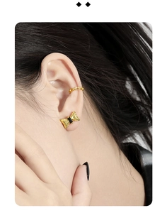 Detail of a golden bow stud earring and chain ear cuff worn on a model's left ear