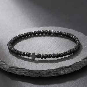 Macro shot of black beads bracelet with a cross pendant resting on a dark stone slab