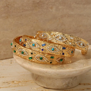 Bracciali aperti dorati malocchio con pietre colorate su vassoio di pietra