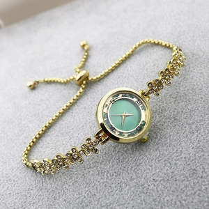 Detail of adjustable gold-tone flower link bracelet watch with shimmering green dial