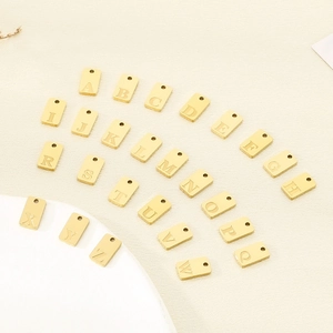 Set of 26 golden stainless steel rectangular alphabet pendants arranged on a soft background