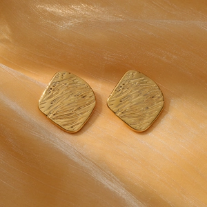 Macro shot of gold square stud earrings with brushed texture on folded silk background