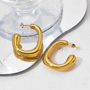 Macro detail of glossy gold-plated chunky U-shaped hoop earrings on reflective surface