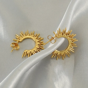 Golden sunburst fan earrings with minimalist ray design on silk fabric background