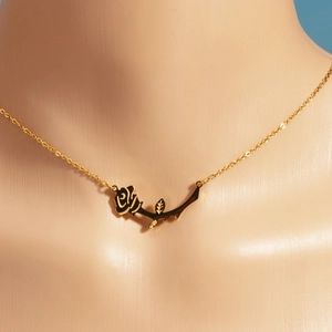 Detail of a vintage black rose pendant on a delicate gold chain worn by a model