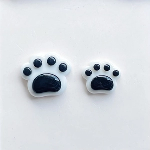 Close-up of black and white resin cat paw charms in two sizes on a minimalist background