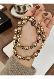 Gros plan d'un collier en perles et œil de tigre avec placage d'or tenu à la main