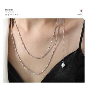 Detail of a silver-tone double-layered snake chain necklace with a drop pearl pendant