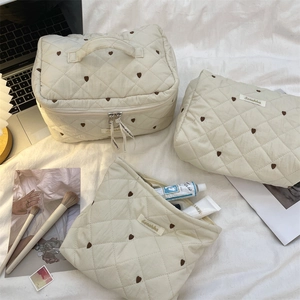 Quilted off-white cosmetic bags set with brown heart patterns on a stylish bed background