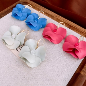 Matte flower earrings with gold hooks in blue, white, and pink on a wooden tray