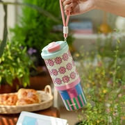 Close-up of a floral pattern drink tumbler with pink lid and strap in a bright room