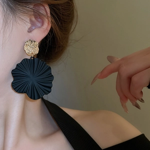 Nahaufnahme von Model mit großen schwarz-goldenen Blumenohrringen und gehämmerter Metallstruktur