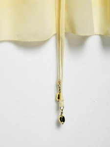 Detail of light yellow summer blouse featuring thin straps and golden teardrop metal charms
