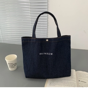 Deep blue denim lunch tote with Rainbow print and metal clasp on a desk with a coffee cup
