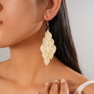 Detail of layered gold metal leaf tassel earrings with textured veins on a female model
