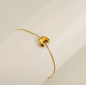 Macro view of gold minimalist letter M balloon pendant on fine cable chain bracelet