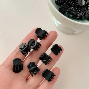 Macro shot of 8 mini black hair clips in hand showing compact size and matte plastic texture