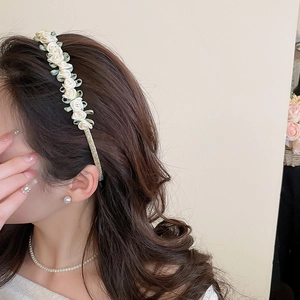 Detailed view of handmade cream satin rose headband with green leaves on wavy hair