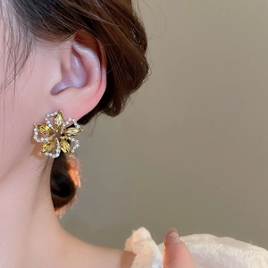Detail view of flower stud earring with yellow marquise stones on a model ear
