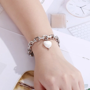 Detail eines silbernen Kettenarmbands mit Herz-Perlenanhänger am Handgelenk des Models