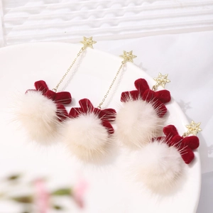 Detailed view of Christmas tree earrings with gold snowflakes, red bows and white pom-poms