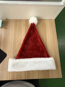 Detail of a red plush Christmas hat with a fluffy white pompom on a wooden surface