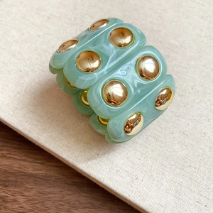 Close-up of mint green resin acrylic bracelet with gold metal studs on beige card