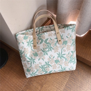 Detail view of floral canvas tote bag with leather handles and natural leaf patterns