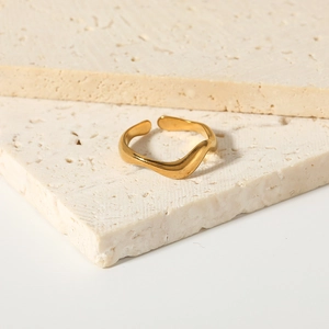 Minimalist wave-shaped gold plated stainless steel open ring on a travertine stone