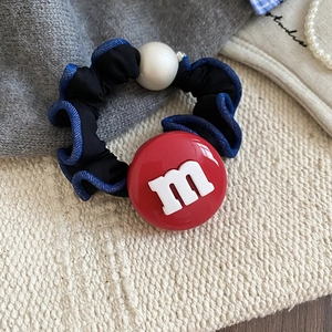 Détail d'un chouchou noir avec une perle rouge lettre m et un accessoire en perle blanche