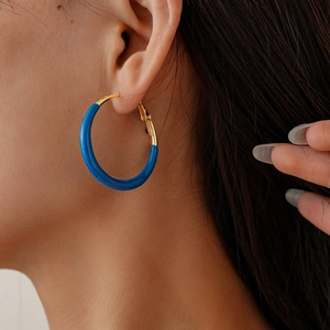 Detail of royal blue enamel hoop earring on model showing polished gold metal finish