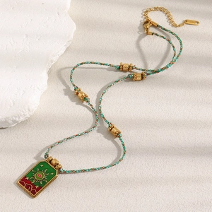 Detail of 18K gold tarot sun necklace with green enamel on a woven cord chain