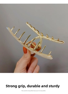 Close-up of a large gold metal hair claw clip with cream pearl accents and strong grip teeth