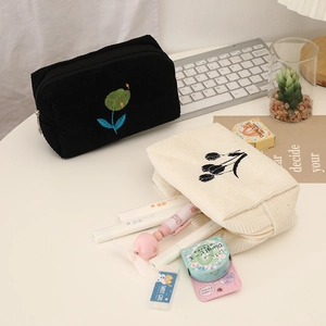 Floral embroidered corduroy cosmetic bags in black and white shown on a desk