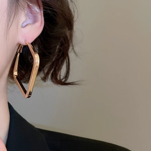 Close-up of oversized geometric gold hoop earrings with a high-polished metallic finish