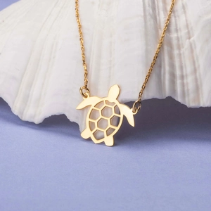 Collier tortue dorée avec carapace hexagonale ajourée sur un fond de coquillage blanc