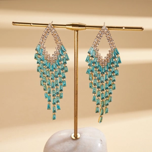 Detail view of gold earrings with blue baguette zircon tassels on a luxury marble stand
