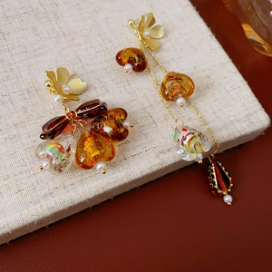 Detail of amber asymmetric tassel earrings with gold floral studs and resin beads