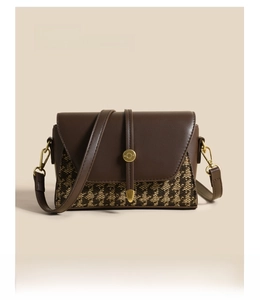 Detail of a brown leather and houndstooth fabric crossbody bag with gold round buckle