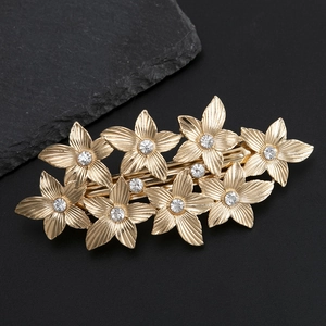 Elegant gold metal flower hair clip with rhinestones shown on a dark stone background