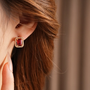 Close-up of elegant gold square earrings with red gemstone and crystal halo on model