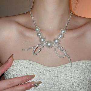 Close-up of model wearing an elegant pearl necklace with a vintage bow design