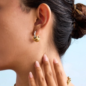 Close-up of dual-tone C-shaped earrings on model with gold rings and silver base