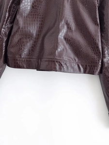 Detailed macro view of dark brown crocodile embossed texture on a shiny faux leather jacket